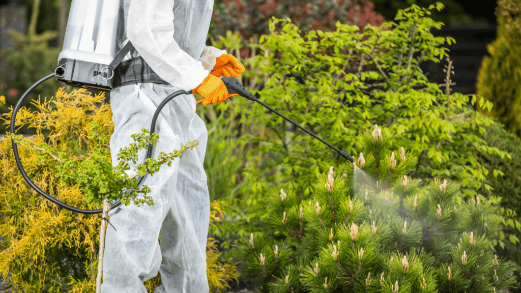Person in protective gear spraying plants with natural pest control solution in a lush garden, emphasizing tick and mosquito protection services in New Jersey.